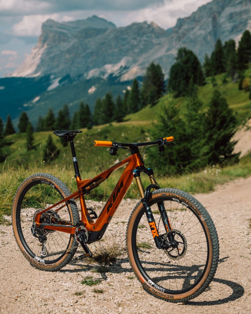 VTT électrique KTM Macina Scarp SX Exonic orange sur sentier de montagne, vue avant trois-quarts