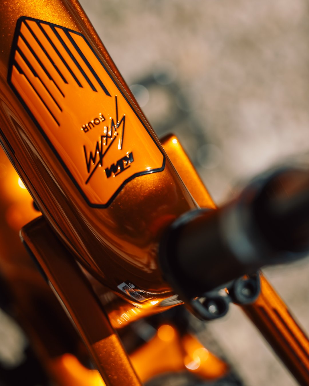 Gros plan sur le cadre du VTT KTM Macina Scarp SX Exonic avec finition orange métallisée et signature stylisée.