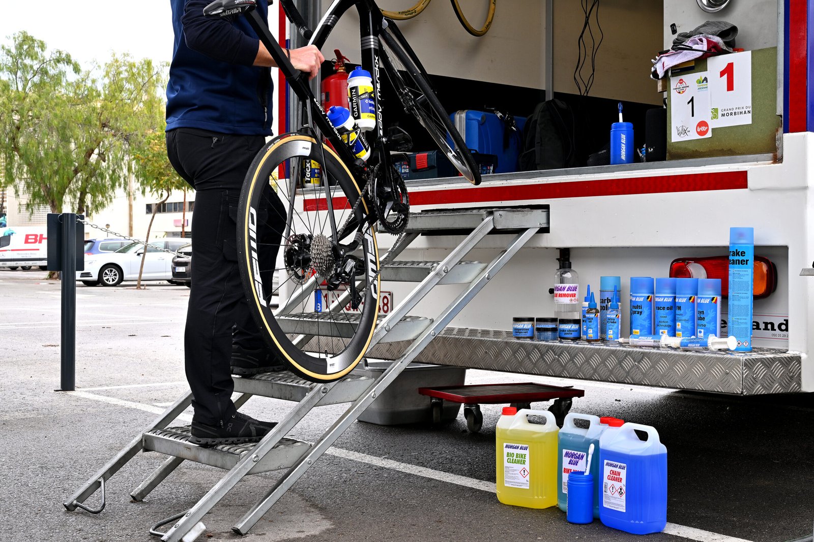 Mécanicien range un vélo sur un rack de service avec divers lubrifiants et nettoyants Morgan Blue