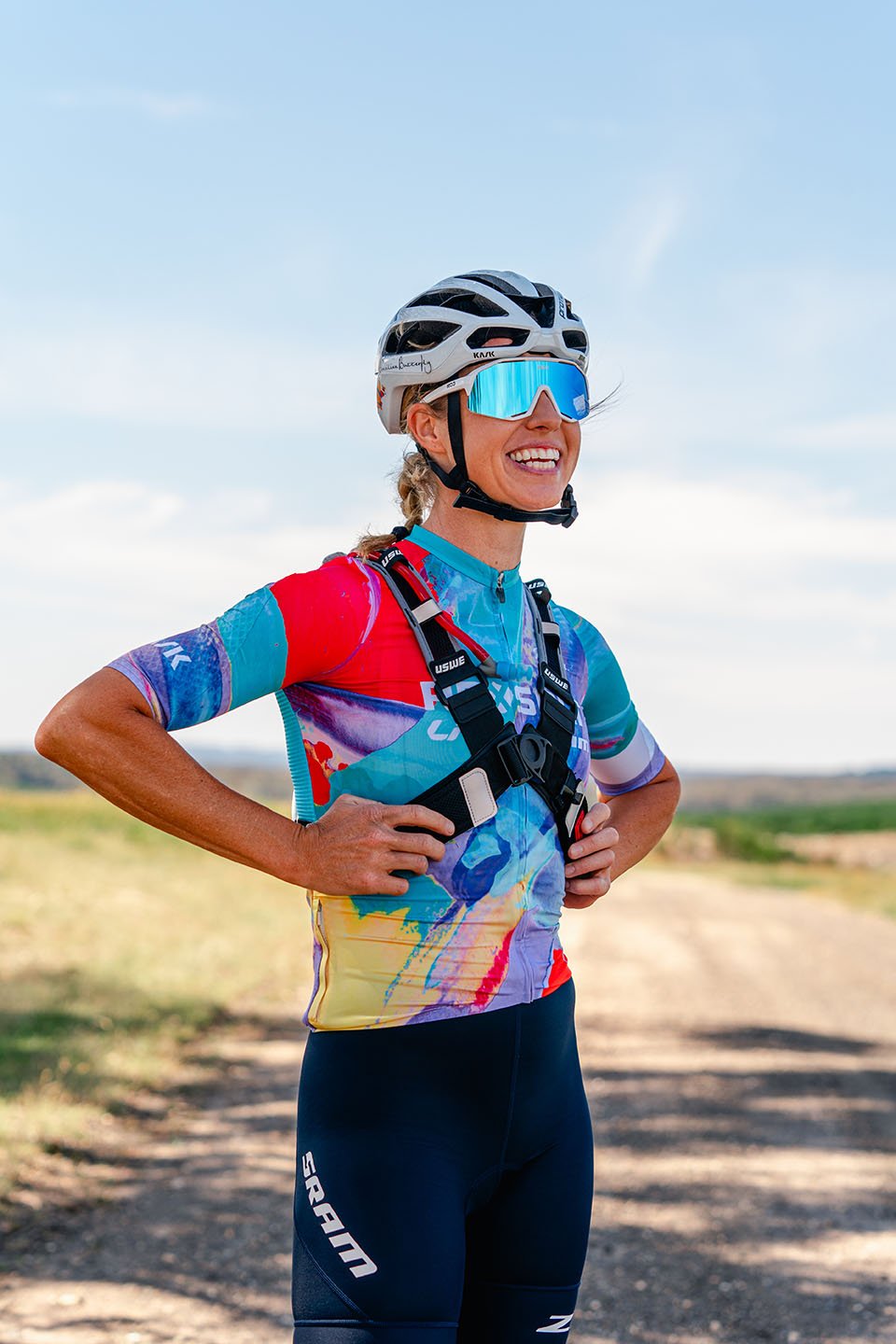 Peta Mullens souriante sur une piste gravel, en tenue colorée, équipée pour la Life Time Grand Prix avec ruban Burgh sur cintre
