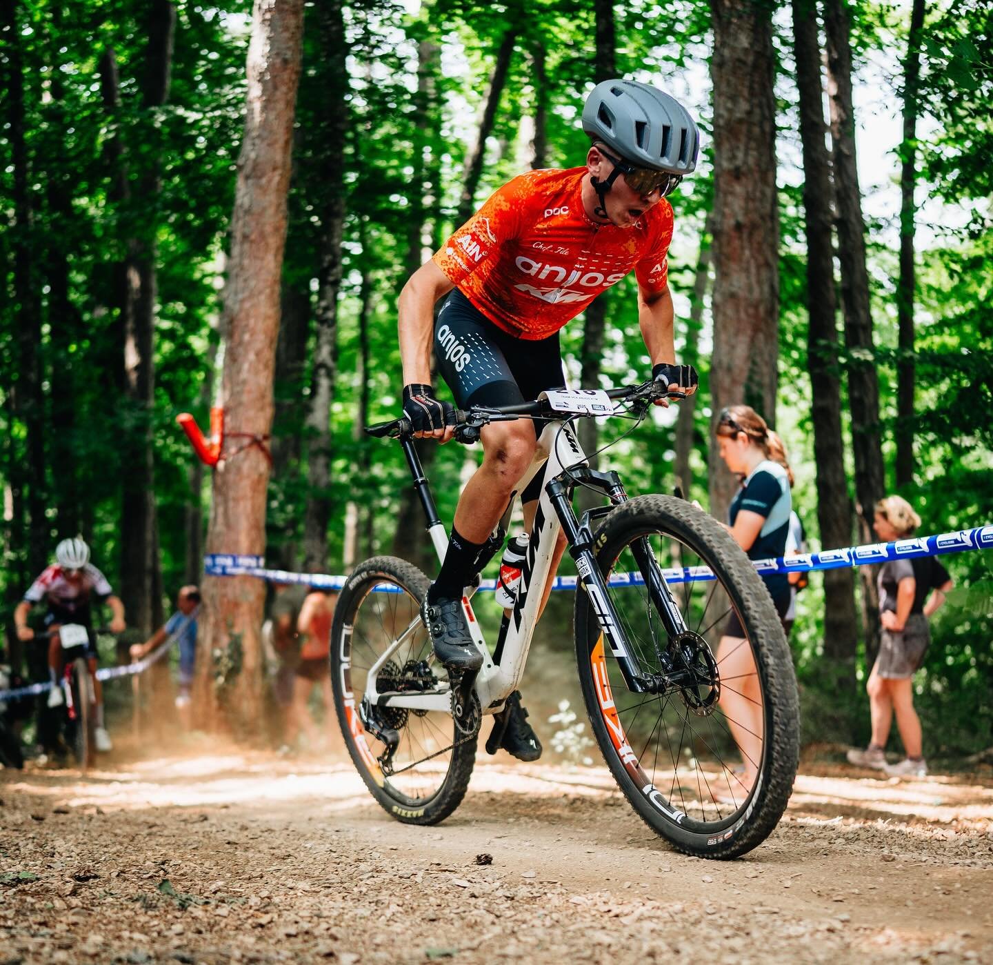 Coureur VTT du Team VCA Anjos KTM en plein effort lors d'une manche de Coupe de France, portant un maillot orange et utilisant un vélo KTM Scarp sponsorisé par Cycling and Sports.