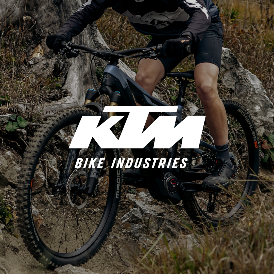 Logo KTM Bike Industries sur une scène de descente VTT en forêt, représentant la performance tout-terrain.